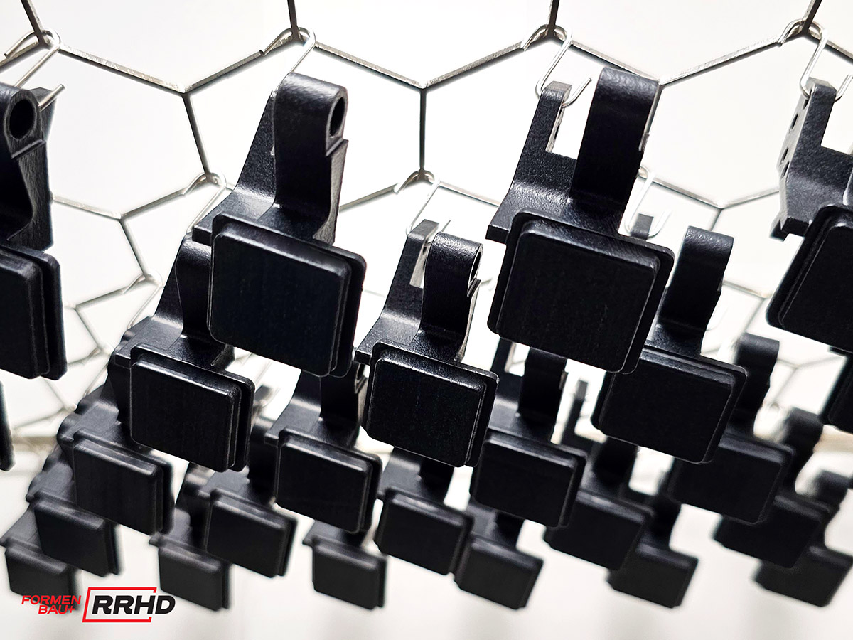 Schwarz glänzende 3D-gedruckte Teile nach dem Vapor-Smoothing-Verfahren, perfektioniert für eine glatte Oberfläche, auf einem hexagonalen Gitter.